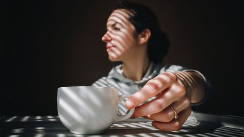 Thema Kopfschmerzen: Eine Frau mit einer Tasse Kaffee vor sich
