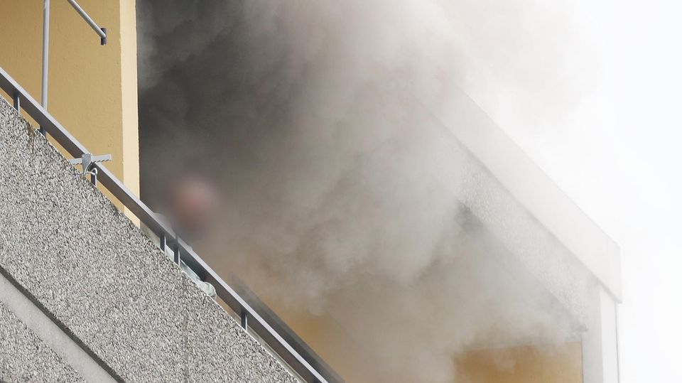 Eine Person steht auf dem Balkon von einem Hochhaus, aus dem Rauch quillt Eine Person steht auf dem Balkon von einem Hochhaus, aus dem Rauch quillt