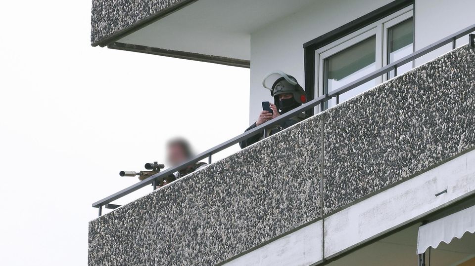Ein Polizeibeamter in Spezialausrüstung steht auf einem Balkon neben einem Kollegen und zielt mit einer Waffe Ein Polizeibeamter in Spezialausrüstung steht auf einem Balkon neben einem Kollegen und zielt mit einer Waffe