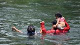Das Kleinkind auf den Schultern, die Frau an der Hand führt ein Mann seine kleine Familie durch das Wasser des Grenzflusses