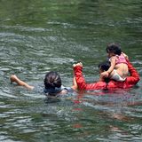 Das Kleinkind auf den Schultern, die Frau an der Hand führt ein Mann seine kleine Familie durch das Wasser des Grenzflusses