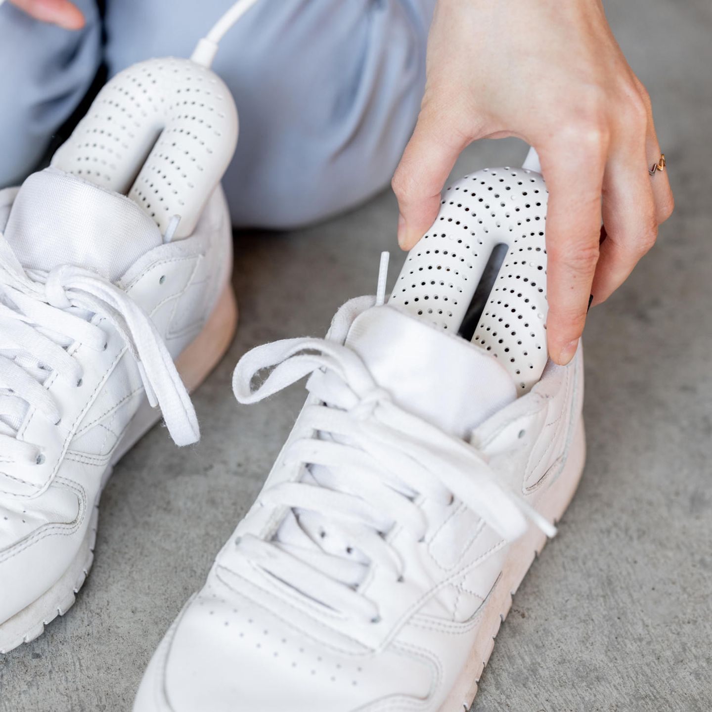 Frau führt elektrischen Trockner in ihre weißen Turnschuhe ein