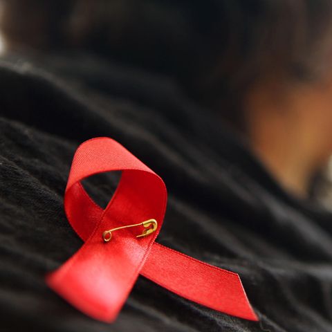Eine Frau hat sich eine rote Schleife angeheftet, ein Zeichen der Solidarität für mit HIV Infizierten