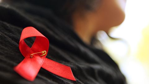 Eine Frau hat sich eine rote Schleife angeheftet, ein Zeichen der Solidarität für mit HIV Infizierten