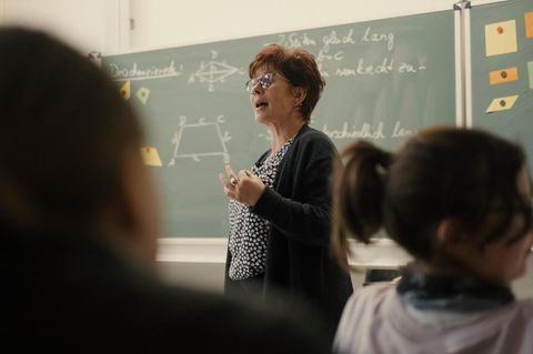 Eine ältere Frau steht vor einer Schulklasse an der Tafel