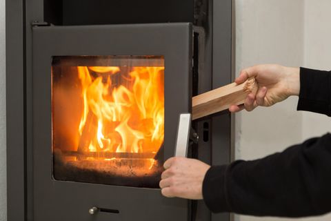 Eine Person legt ein Stück Holz in einen Kaminofen