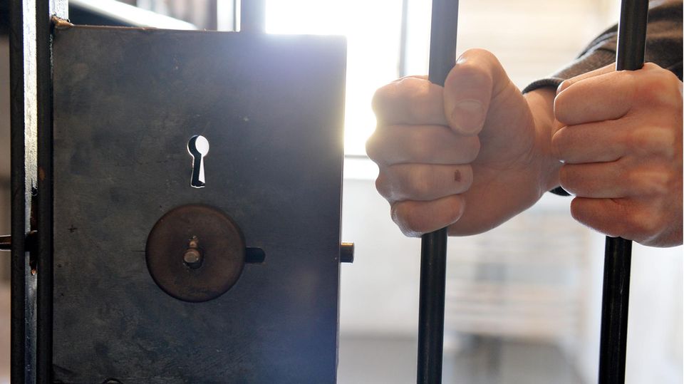 Eine Häftling umgreift die Gitterstäbe einer Tür. Großbritannien will Häftlinge aus dem Gefängnis abschieben.