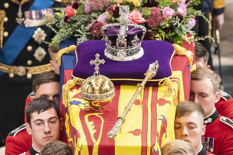 Sechs weiße Männer in roten Uniformjacken tragen den von einer Flagge bedeckten Sarg von Queen Elizabeth II.