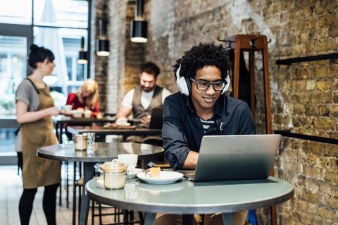 Junger Mann sitzt mit Laptop und Laptopzubehör in einem Café