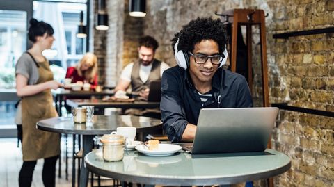 Junger Mann sitzt mit Laptop und Laptopzubehör in einem Café