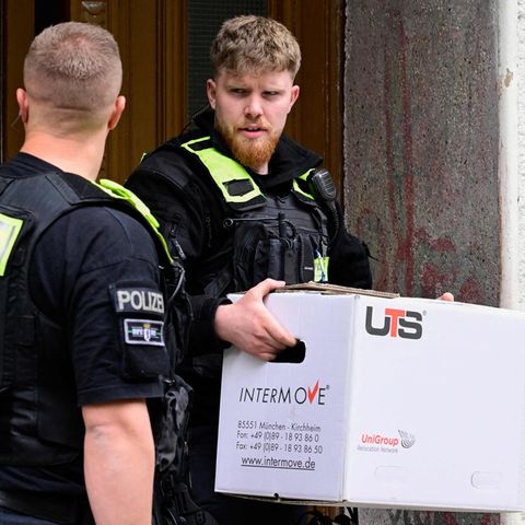 Ein Polizist trägt nach der Razzia gegen die "Letzte Generation" einen Karton aus einem Haus in Berlin-Kreuzberg