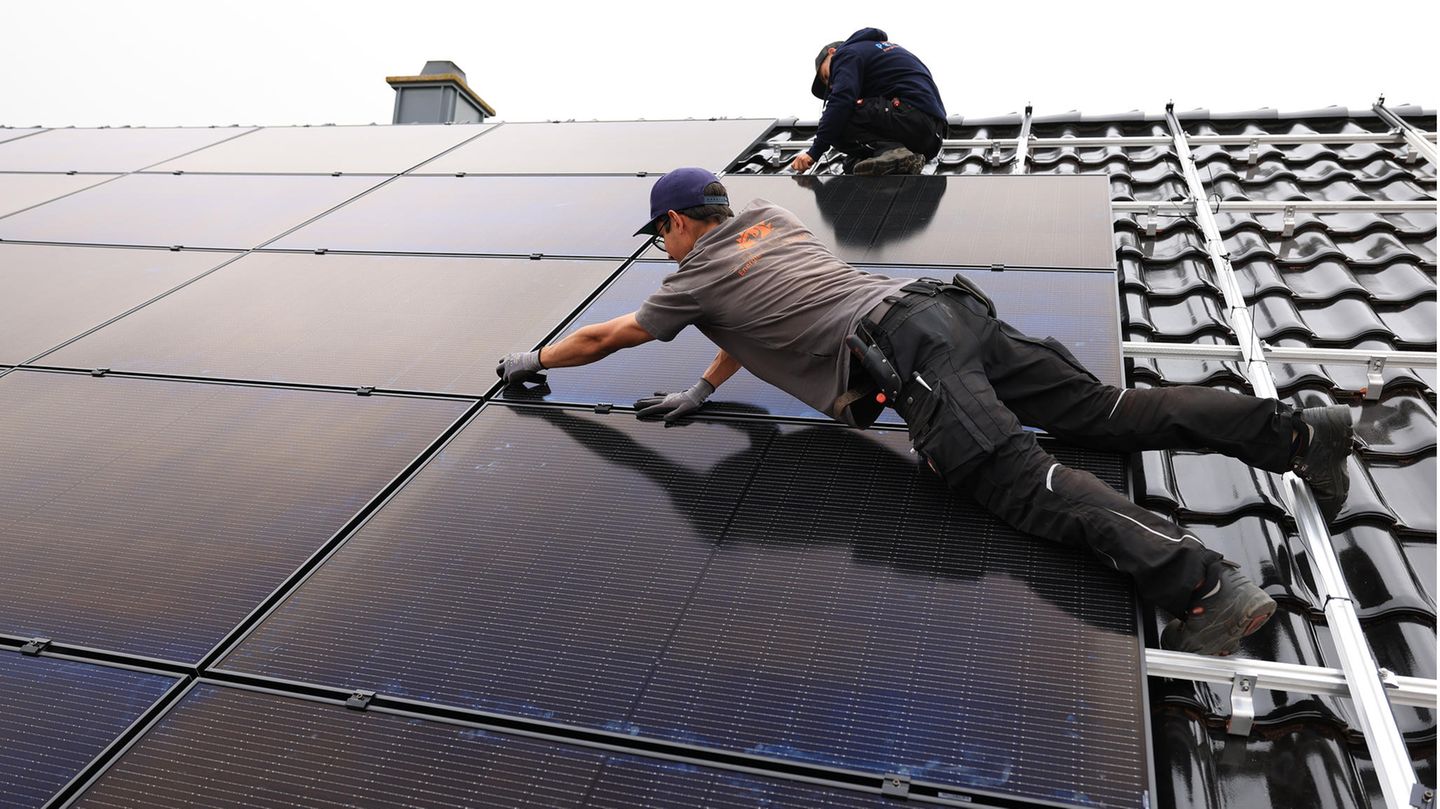 Fachkräftemangel: Handwerker montieren auf dem Dach eines Wohnhauses Solarmodule