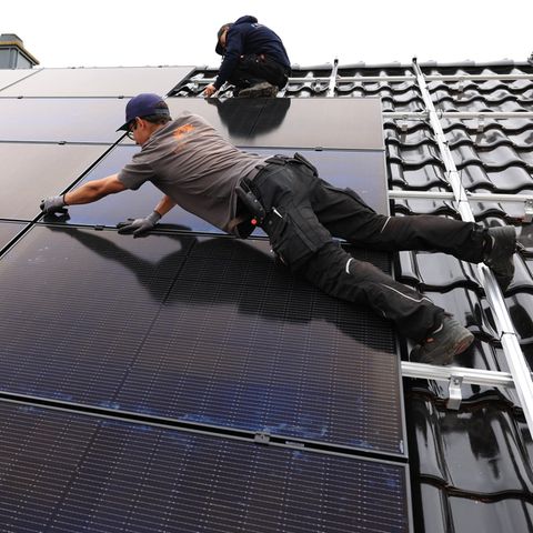 Fachkräftemangel: Handwerker montieren auf dem Dach eines Wohnhauses Solarmodule