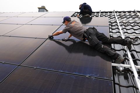 Fachkräftemangel: Handwerker montieren auf dem Dach eines Wohnhauses Solarmodule