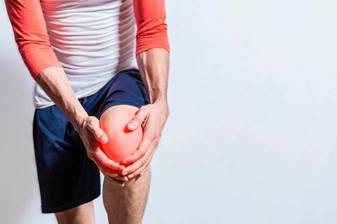 Ein Sportler hält sich das schmerzende Knie mit den Händen