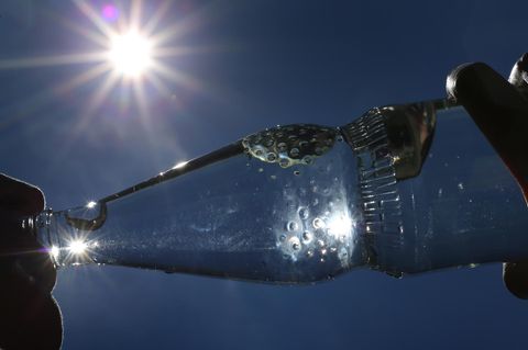 Eine Person trinkt aus einer Flasche Mineralwasser, die Sonne scheint