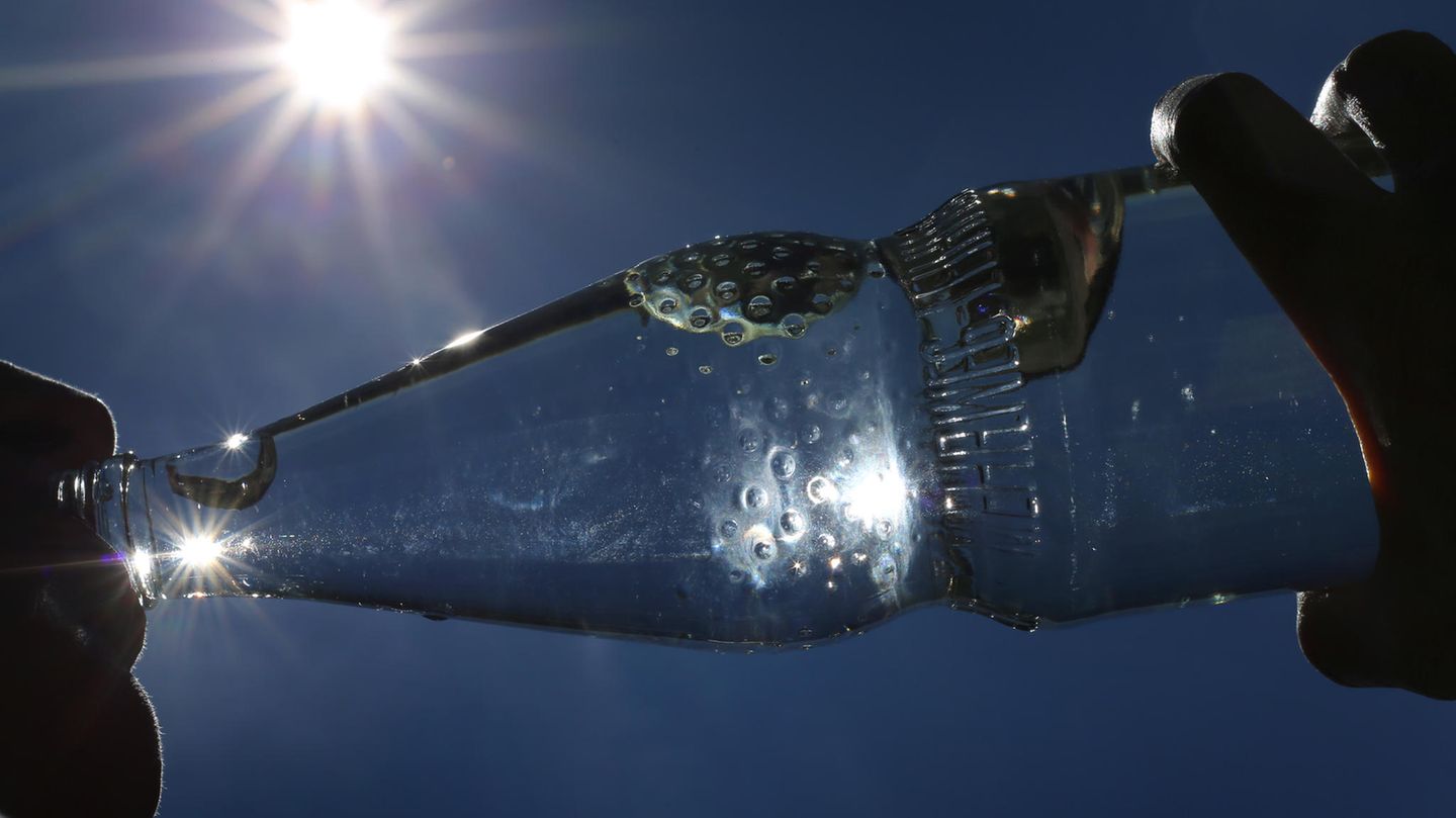 Eine Person trinkt aus einer Flasche Mineralwasser, die Sonne scheint