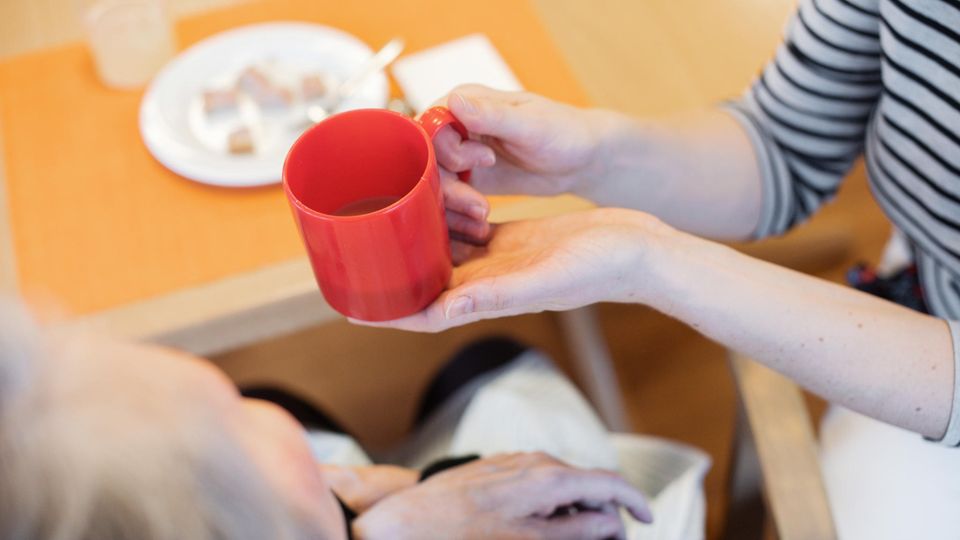 Eine Pflegerin reicht einer Frau ein Getränk.