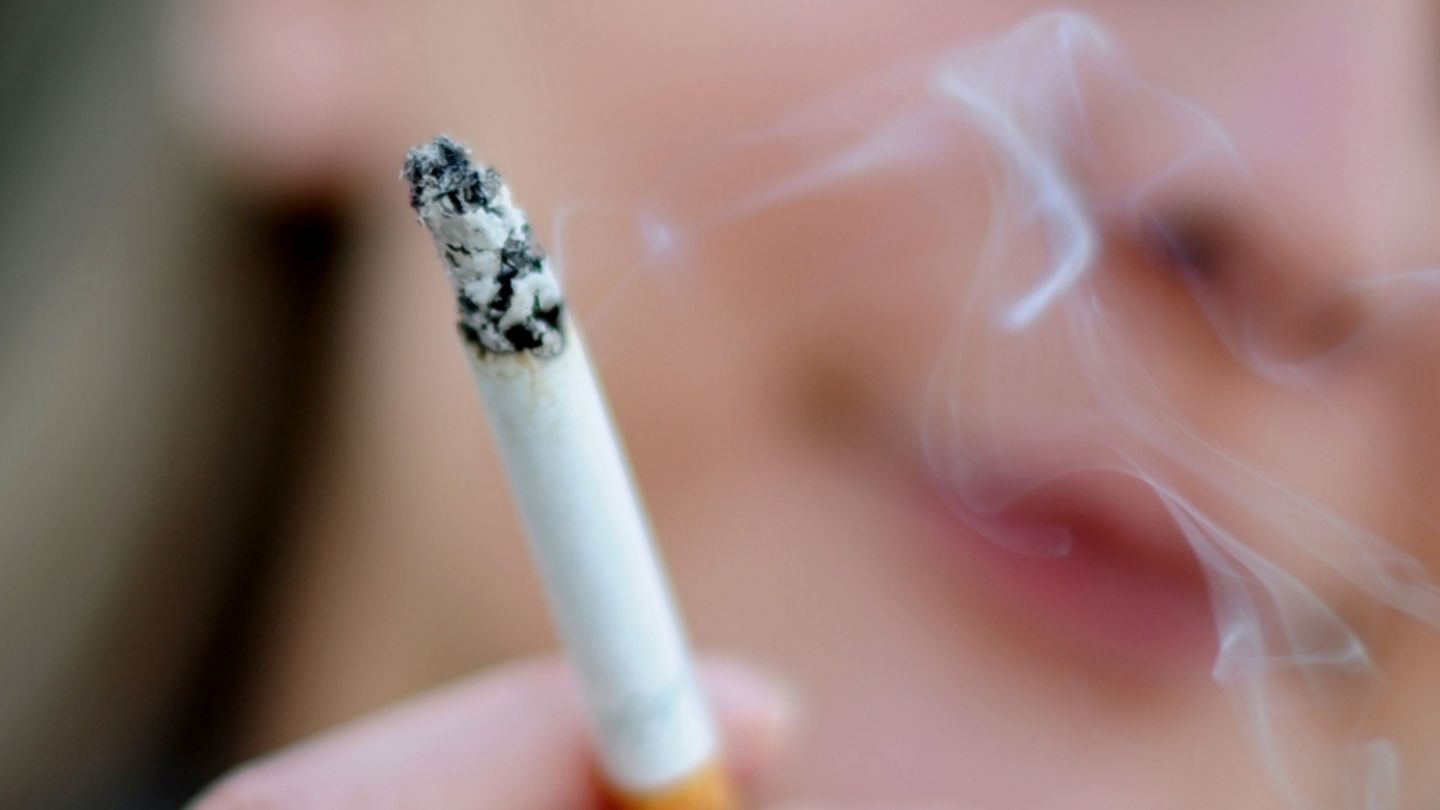 Rauchen: Rauch steigt von der Glut einer Zigarette auf, die eine junge Frau in der rechten Hand hält