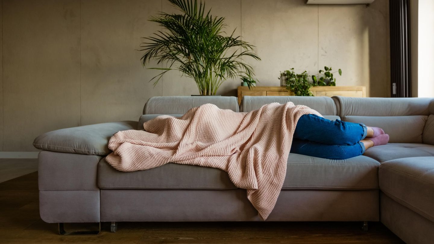 Eine Frau mit Migräne liegt unter der Decke auf dem Sofa