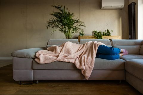 Eine Frau mit Migräne liegt unter der Decke auf dem Sofa