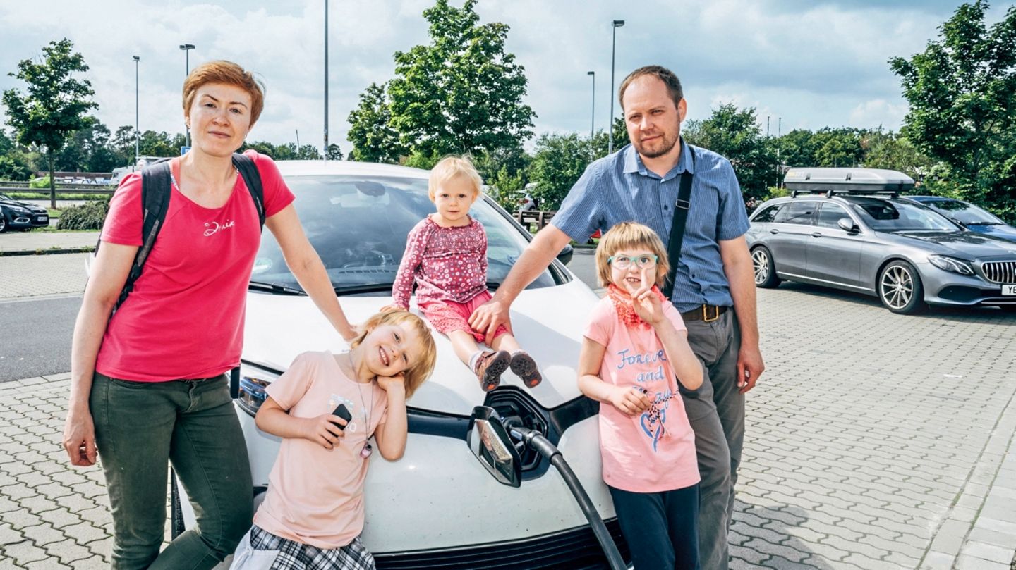 Eltern mit drei Kindern stehen vor einem Elektroauto das geladen wird