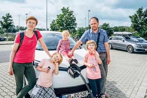 Eltern mit drei Kindern stehen vor einem Elektroauto das geladen wird