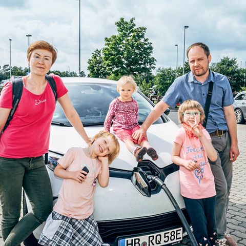 Eltern mit drei Kindern stehen vor einem Elektroauto das geladen wird