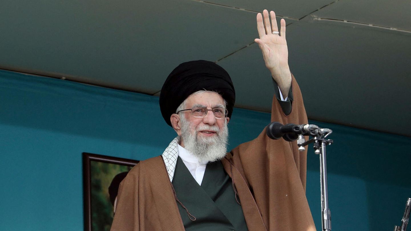 Ali Khamenei Ali Khamenei steht am offenen Fenster vor einem Mikrofon und winkt mit seiner linken Hand. Er trägt einen schwarzen Turban
