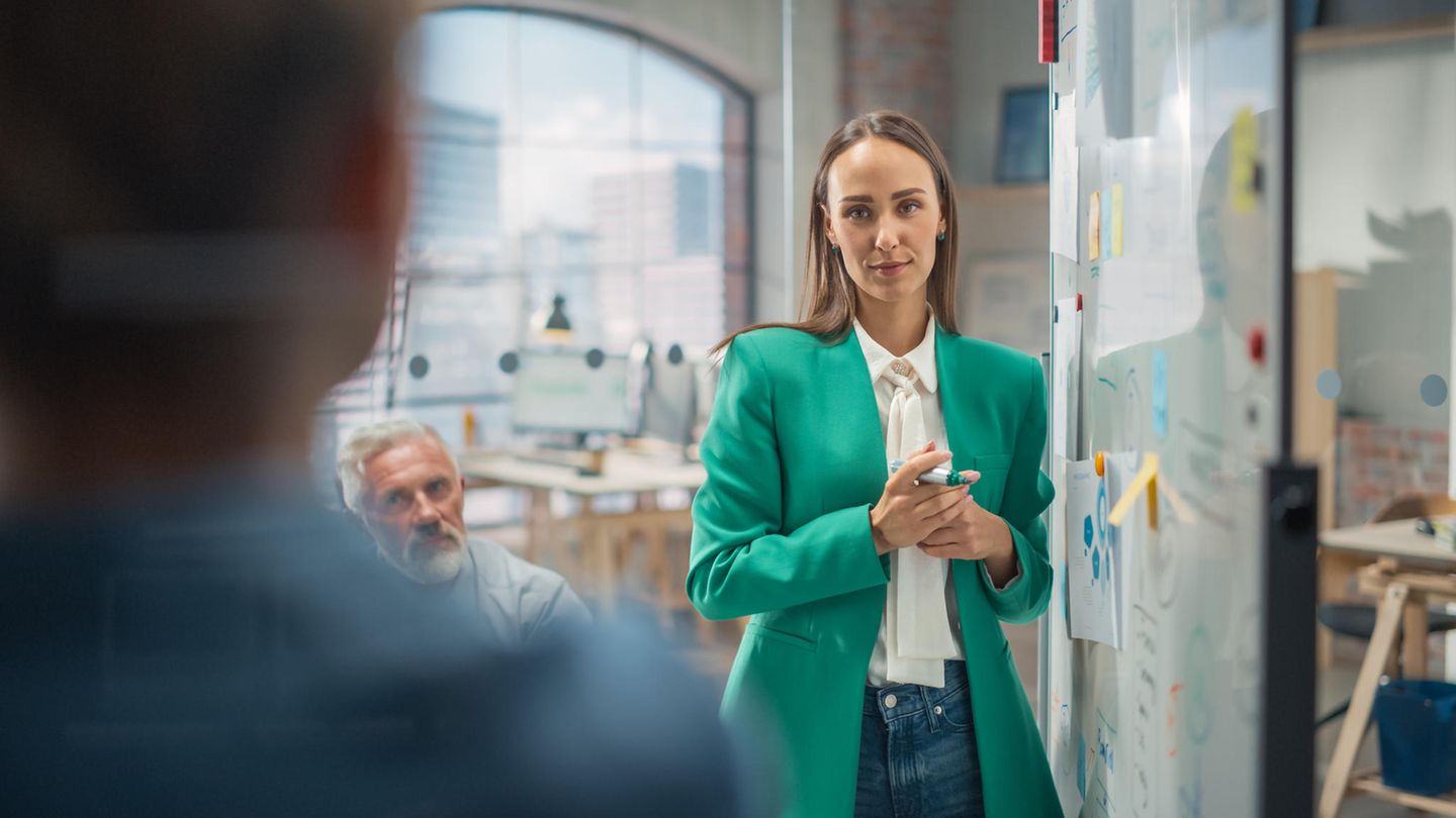 Eine Frau steht in einem Büro – umgeben von zwei Männern.