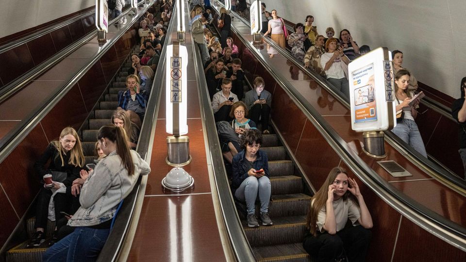 Menschen sitzen auf einer Rolltreppe während sie in einer Metrostation in Kiew Schutz suchen
