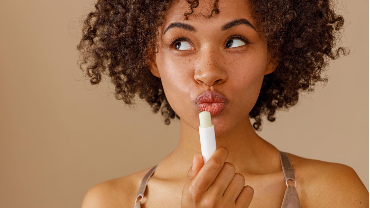 Eine Frau macht einen Kussmund und hält einen Lippenstift in der Hand.