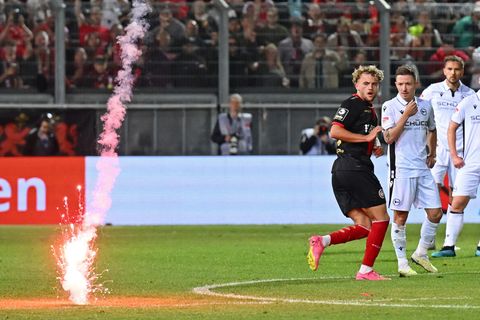 Eine rote Rakete schlägt neben Profi-Fußballern von Wehen Wiesbaden und Arminia Bielefeld auf dem Rasen ein