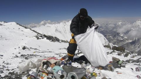 Ein Mensch in warmer Kleidung sammelt am Mount Everest Müll in einen weißen Sack