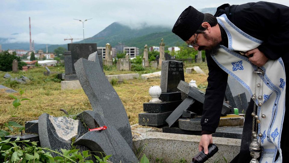 Ein orthodoxer Priester hält über einem vandalisierten Grab einen Gedenkgottesdienst ab
