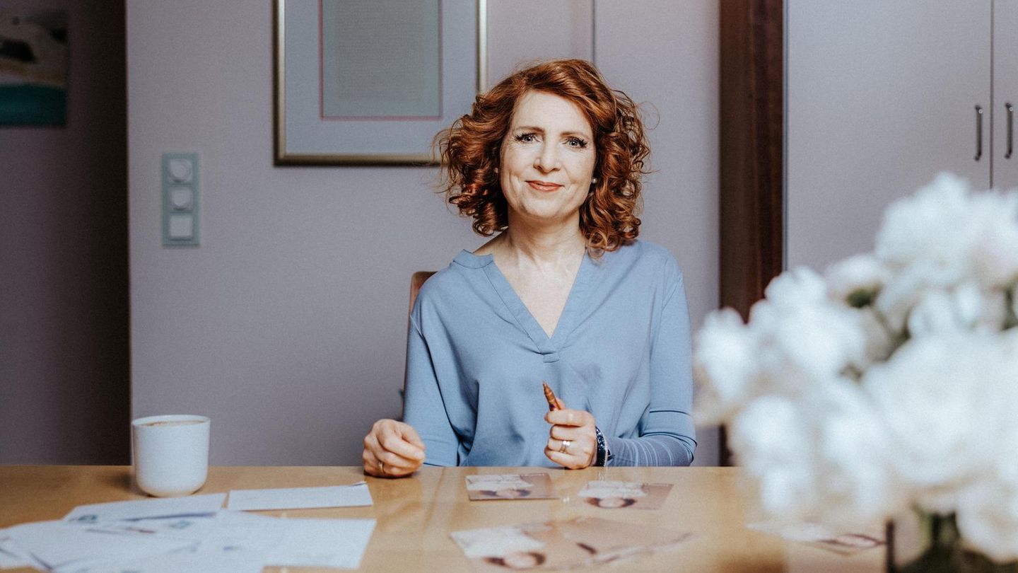 Monica Lierhaus sitzt an einem Tisch und signiert Autogrammkarten