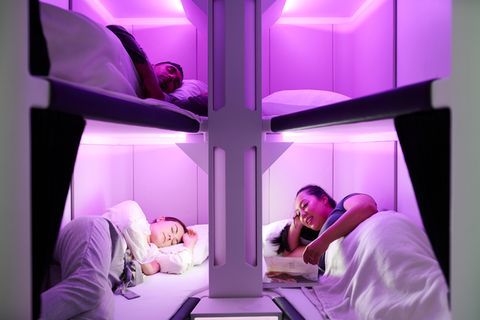 Drei Menschen liegen in einer violett beleuchteten Schlafkabine – das "Skynest" von Air New Zealand.