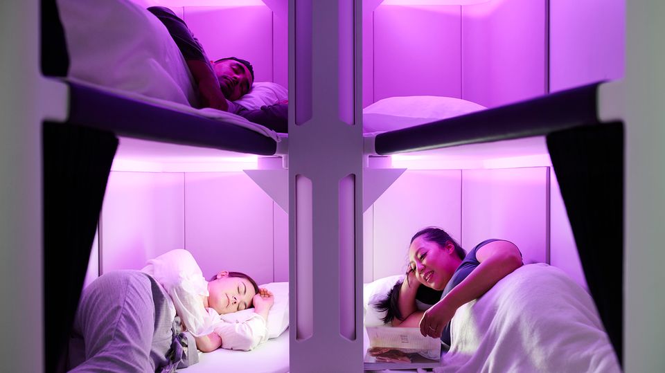 Drei Menschen liegen in einer violett beleuchteten Schlafkabine – das "Skynest" von Air New Zealand.