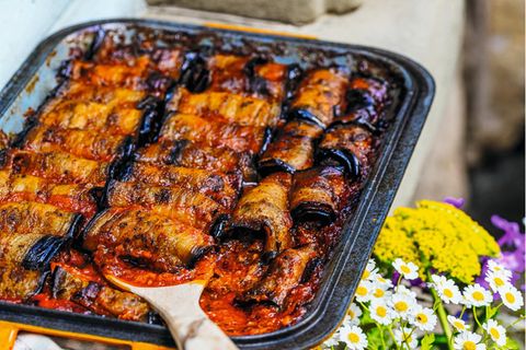 Auberginenröllchen mit Hackfleisch      Zutaten:  3 große Auberginen  Salz, Pfeffer aus der Mühle  120 ml Olivenöl extra vergine  1 TL edelsüßes Paprikapulver  1 TL getrockneter Oregano  1 TL gemahlener Kreuzkümmel  2 Zwiebeln  2 Knoblauchzehen  700 g Rinderhackfleisch  30 g Petersilie, fein gehackt  2 Prisen Zimt  500 G reife Tomaten  150 ml Rotwein      Zubereitung:  1. Den Backofen auf 190 Grad Umluft vorheizen.  2. Die Auberginen längs in etwa 1½ cm dicke Scheiben schneiden und in eine Schüssel geben. Mit Salz und Pfeffer bestreuen, dann 30 ml Olivenöl sowie je 1 Prise Paprikapulver, Oregano und Kreuzkümmel dazumischen.  3. Die Auberginen auf einem Blech verteilen und im vorgeheizten Backofen rund 25 Minuten backen.  4. Die Zwiebeln und den Knoblauch fein hacken. In einer Schlüssel das Hackfleisch mit Zwiebeln, Knoblauch, Petersilie, 40 ml Olivenöl, jeweils restlichem Kreuzkümmel, Paprikapulver und Oregano sowie Zimt, Salz und Pfeffer gut vermischen und etwa 5 Minuten kneten.  5. Jeweils 1 Esslöffel der Hackfleischfüllung auf die untere schmale Seite jeder gebackenen Auberginenscheibe geben und die Scheiben aufrollen. So lange fortfahren, bis alle Zutaten aufgebraucht sind.  6. Die Tomaten in Würfel schneiden und auf den Auberginen verteilen. Mit dem restlichen Olivenöl und dem Rotwein begießen. Im Backofen bei 185 Grad  7. Umluft etwa 30 Minuten backen.