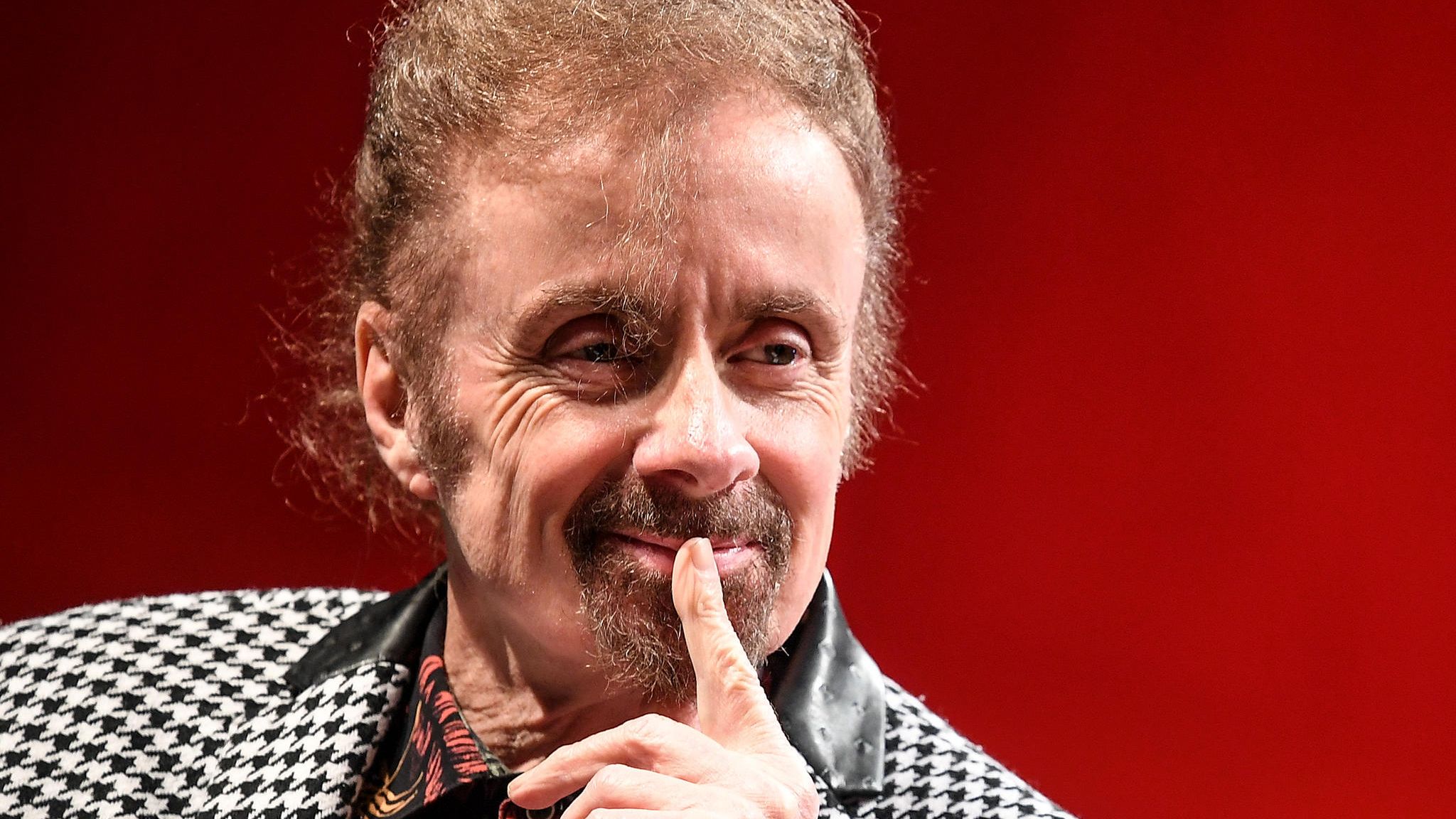 T. C. Boyle hält einen Finger an die Lippen und lächelt