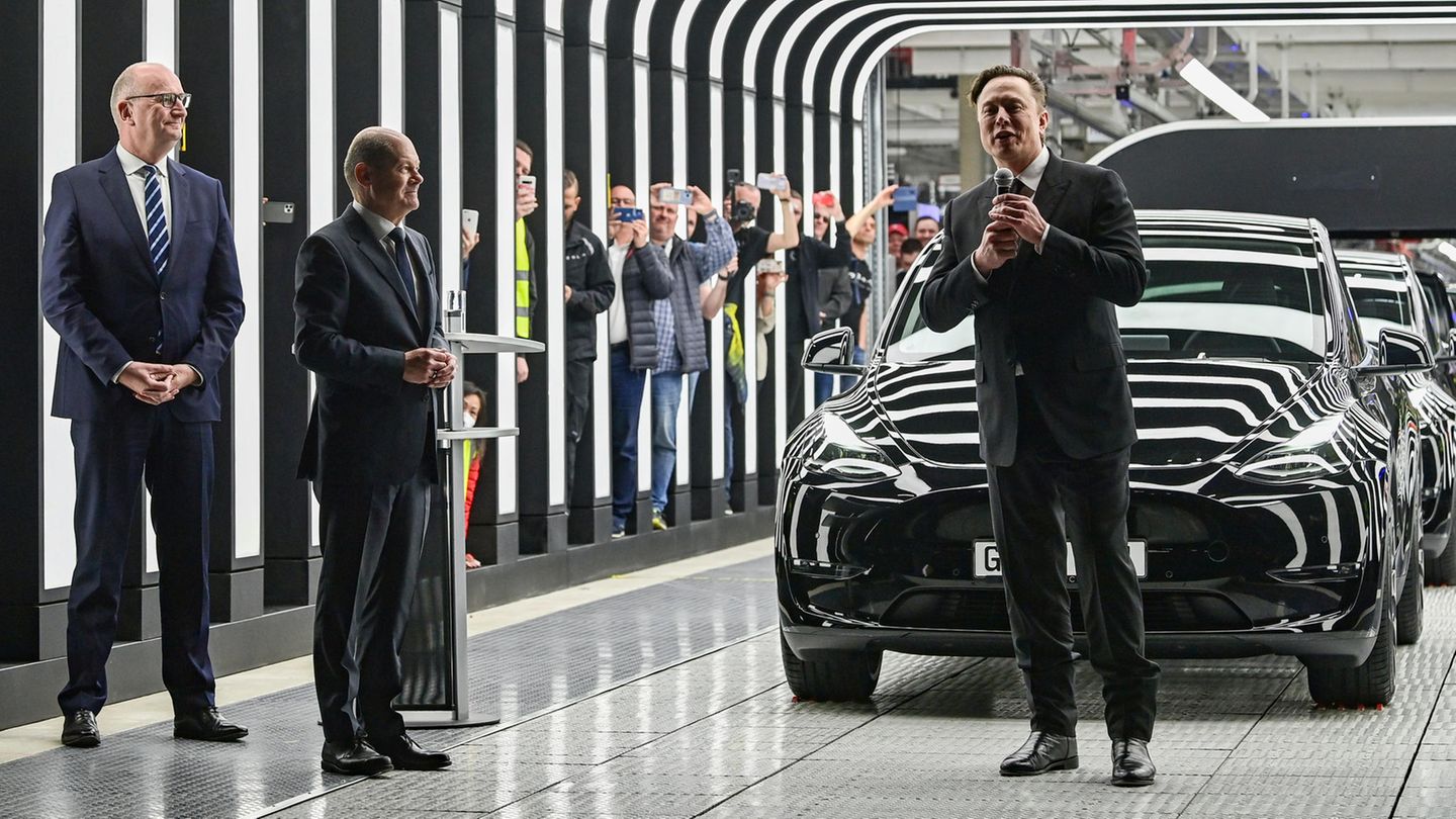 Dietmar Woidke, Olaf Scholz und Elon Musk stehen vor einem Auto in der Tesla-Fabrik in Brandenburg