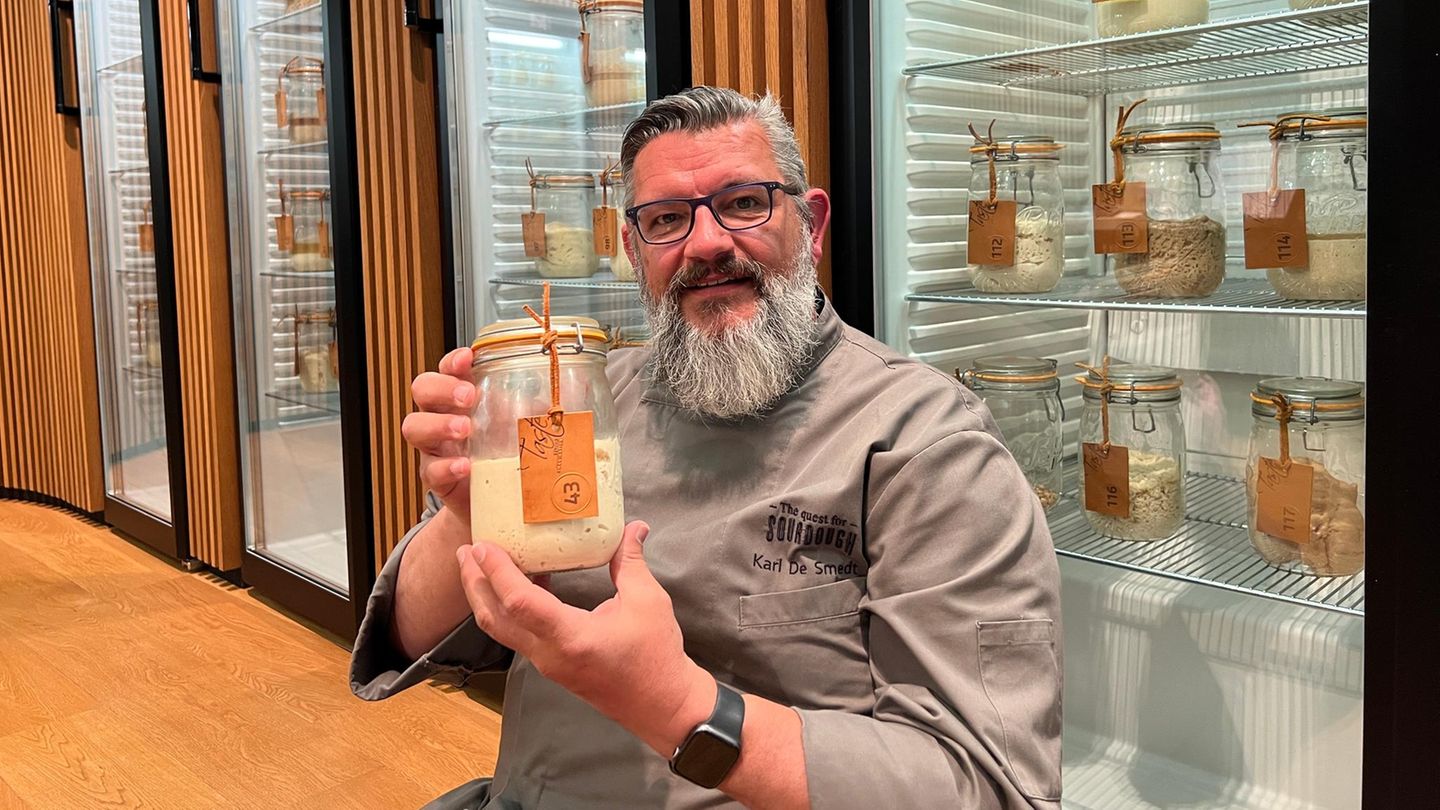 Karl de Smedt hält ein Glas mit Sauerteig, hinter ihm Kühlschränke mit mehr Sauerteig-Gläsern