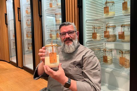 Karl de Smedt hält ein Glas mit Sauerteig, hinter ihm Kühlschränke mit mehr Sauerteig-Gläsern