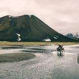 Ein Mann fährt auf Island durch einen Fluss und bekommt nasse Füsse