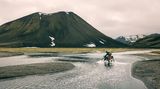 Ein Mann fährt auf Island durch einen Fluss und bekommt nasse Füsse