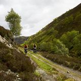 Zwei Männer radeln durch die schottischen Highlands, die grün bewachsen sind