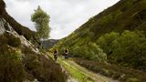 Zwei Männer radeln durch die schottischen Highlands, die grün bewachsen sind