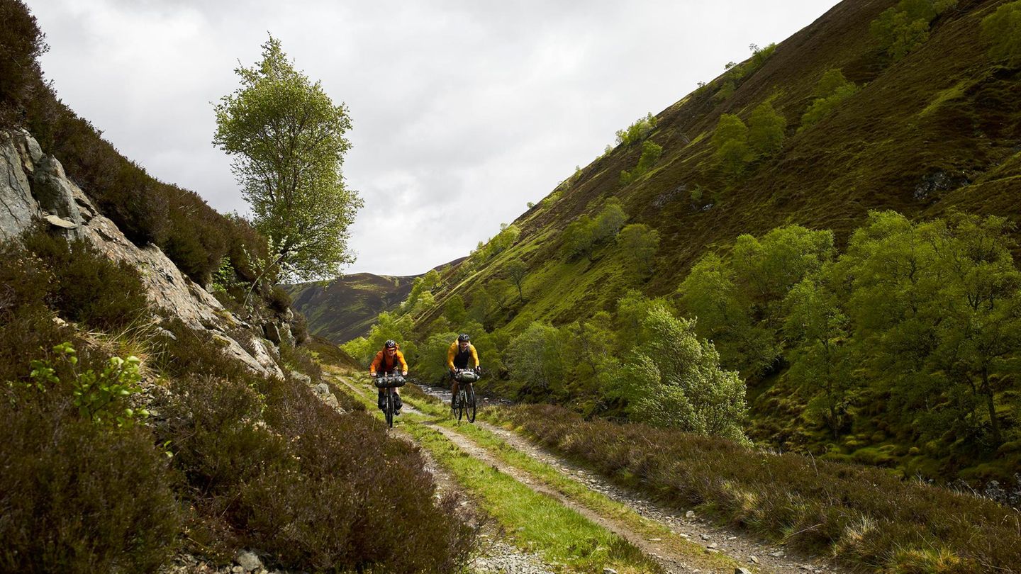 Zwei Männer radeln durch die schottischen Highlands, die grün bewachsen sind
