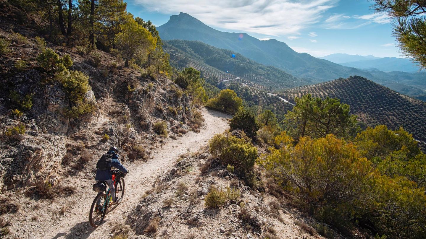 Ein Radfahrer fährt durch die Berge in Andalusiens, in der Ferne ragt ein Gipfel heraus