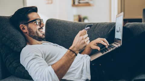 Amazon Sterne-Shop: Mann liegt mit Kreditkarte und Laptop auf einem Sofa